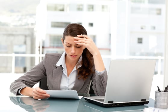 Pensive businesswoman looking at a paper while working on her laptop at her desk